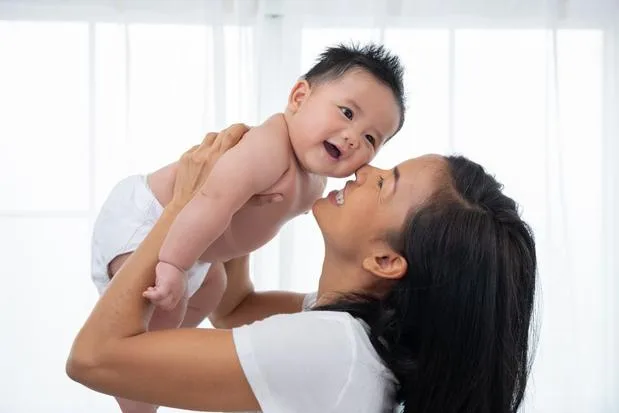 Ibu tersenyum bahagia sambil menggendong bayinya yang baru lahir